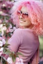 Close-up portrait of pretty young woman with curly pink hair and sunglasses near the blossoming spring tree. Royalty Free Stock Photo