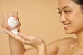 Close up portrait of pretty young woman smiling, holding a bottle of gentle foam facial cleanser isolated over beige Royalty Free Stock Photo