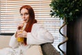 Close-up portrait of pretty young woman in white bathrobe drinking cocktail from straw sitting on sofa by window at spa Royalty Free Stock Photo