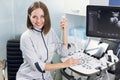 Close up portrait of professional smiling young woman doctor sonographer sitting near modern ultrasound scanner machine Royalty Free Stock Photo