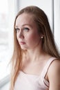 Close-up portrait of real candid beautiful woman with gray eyes and long hair, looking out the window Royalty Free Stock Photo