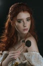 A close-up portrait of a red-haired young woman in a vintage gold dress with bare shoulders with a dry bouquet in hands on a black Royalty Free Stock Photo