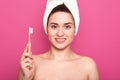Close up portrait of refreshed female with European woman holds toothbrush in hand, poses with naked shoulders, wrapped white