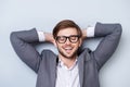 Close-up portrait of relaxing handsome young man with bristle and spectacles in formal wear holds hands behind head and