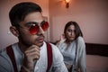 Close-up portrait of a sad brooding brunette guy in sunglasses. in the background on the bed a young brunette girl. selective