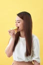 Close up portrait of a satisfied pretty girl eating donuts over yellow background