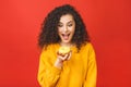 Close up portrait of a satisfied pretty young girl eating donuts isolated over red background