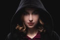 Close-up portrait of a secretive young girl in a deep dark hood on a black background. The concept of secrecy of secrets