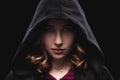 Close-up portrait of a secretive young girl in a deep dark hood on a black background. The concept of secrecy of secrets