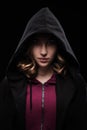 Close-up portrait of a secretive young girl in a deep dark hood on a black background. The concept of secrecy of secrets