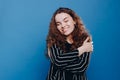 Close up portrait of self confident curly woman hugging herself and smiling happily isolated on blue background. Self love and Royalty Free Stock Photo