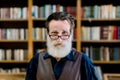 Close up portrait of senior man with beard and eyeglasses, looking at camera, standing on book shop market background Royalty Free Stock Photo