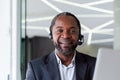 Close-up portrait of a senior smiling African-American man working in an office using a laptop in a headset and smiling Royalty Free Stock Photo