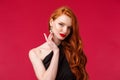 Close-up portrait of sensual seductive redhead woman with red lipstick, touching earring coquettish look camera