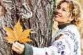 Close up portrait of serene expression woman hugging a tree and holding a yellow leaf enjoying outdoor leisure activity alone in Royalty Free Stock Photo