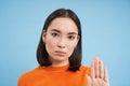 Close up portrait of serious asian woman, shows stops sign, disapproves something, refuses or rejects, stands over blue
