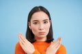 Close up portrait of serious asian woman, shows stops sign, disapproves something, refuses or rejects, stands over blue