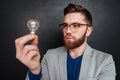 Serious bearded young man standing and looking at light bulb Royalty Free Stock Photo