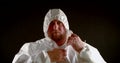 Close-up portrait of a serious, stern, bald, middle-aged man wearing a white suit with a zip-up hood. It is in the