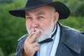 Close up portrait of serious stylish fashion old mature senior in leather coat and fashion hat smoking outdoor. Older Royalty Free Stock Photo