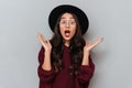 Close-up portrait of shocked attractive woman in glasses and black hat standing with opened palms, looking at camera