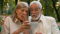 Close up portrait shocked worried aged pensioners man woman old Caucasian couple sitting bench looking phone screen Royalty Free Stock Photo