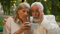 Close up portrait shocked worried aged pensioners man woman old Caucasian couple sitting bench looking phone screen Royalty Free Stock Photo