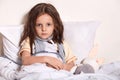 Close up portrait of sick girl in hospital bed, looking at camera, having upset look, feels unwel, taking temperature, laying in Royalty Free Stock Photo