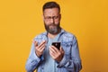Close up portrait of single handsome Caucasian middle aged man in casual T shirt and denim jacket, texting using smartphone and Royalty Free Stock Photo