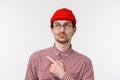 Close-up portrait skeptical and doubtful handsome bearded guy in red beanie, checked shirt and glasses, smirk