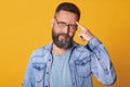 Close up portrait of smart handsome middle aged Caucasian man thinks with finger on head  on yellow background, wears Royalty Free Stock Photo