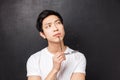 Close-up portrait of smart young asian male student, thinking, touching lip with rim of glasses and looking up Royalty Free Stock Photo