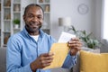 Close-up portrait of a smiling African-American man sitting at home and holding an open envelope with a letter in his Royalty Free Stock Photo