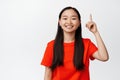 Close up portrait of smiling asian woman pointing finger up, showing advertisement and looking happy at camera Royalty Free Stock Photo