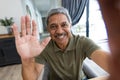 Close-up portrait of smiling biracial senior man waving hand while talking over video call