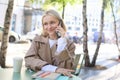 Close up portrait of smiling blond woman, sitting at table outside cafe, talking on mobile phone, having happy, lively Royalty Free Stock Photo
