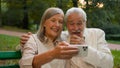 Close up portrait smiling Caucasian middle aged retired family couple talking relaxing using smartphone outdoors city Royalty Free Stock Photo