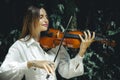 Close up portrait of smiling Caucasian woman playing violin in tropical forest. Closed eyes. Music and art concept. Female wearing Royalty Free Stock Photo