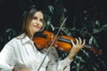 Close up portrait of smiling Caucasian woman playing violin in tropical forest. Music and art concept. Female with blond hair Royalty Free Stock Photo