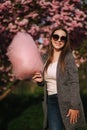 Close up portrait of smiling girl holding cotton candy in hands. Girl dressed in grrey blazer and sunglasses