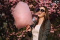 Close up portrait of smiling girl holding cotton candy in hands. Girl dressed in grrey blazer and sunglasses