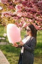 Close up portrait of smiling girl holding cotton candy in hands. Girl dressed in grey blazer and sunglasses