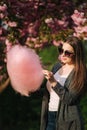 Close up portrait of smiling girl holding cotton candy in hands. Girl dressed in grey blazer and sunglasses