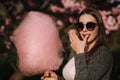 Close up portrait of smiling girl holding cotton candy in hands. Girl dressed in grrey blazer and sunglasses. Girl