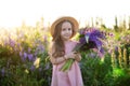 Close up portrait of a smiling little girl in a straw hat and with a large bouquet of lupins. A child girl in a field of lupines. Royalty Free Stock Photo