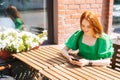 Close-up portrait of smiling pretty young woman using typing mobile phone sitting at table in outdoor cafe terrace in Royalty Free Stock Photo