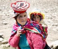 Close up portrait of a smiling Quechua woman dressed in colorful traditional handmade outfit and carrying her baby in a sling