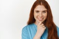 Close up portrait of smiling redhead girl, looking thoughtful, touch chin and gazing at camera, ponder smth, listening