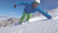 CLOSE UP, PORTRAIT: Smiling snowboarder doing hand drag in fresh powder snow