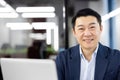 Close-up portrait of a smiling and successful young Asian man in a business suit sitting in the office in front of a Royalty Free Stock Photo